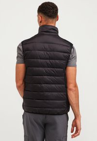 Chaleco acolchado negro con cuello alto, que presenta costuras horizontales y un material ligero. La vista posterior muestra una silueta aerodinámica.