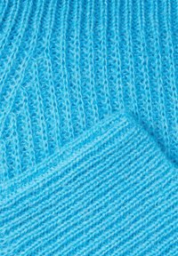 Svetlo modra pletenina z teksturiranim vzorcem. Ima rebraste in gladke sekcije, ki prikazujejo različne vrste šivanja in globino.