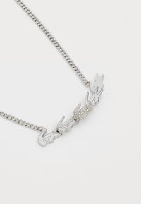 Collier en métal argenté avec un design en maillons présentant des formes animales stylisées et des accents en cristal transparent, monté sur une chaîne en maillons.