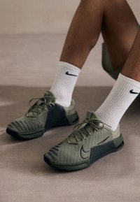 Grønne sportsko med mesh-overdel, teksturerede detaljer og sorte såler. Sammen med hvide ribbede sokker med et sort logo.