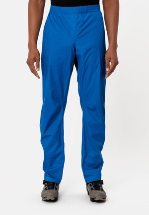 Pantaloni da esterno blu impermeabili, con cintura elastica, gambe affusolate, tessuto leggero, texture liscia, abbinati a robuste scarpe da trekking grigie.