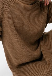 Hnědý pletený svetr s ribovanou strukturou a volným střihem. Výstřih je široký a rukávy jsou mírně oversized.