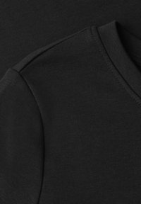 Gros plan d’un tissu en coton noir montrant les détails des coutures d’un col rond et de la zone épaule d’un vêtement.