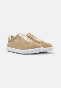Beige sneakers with a smooth textile upper, white laces, contrasting white sole, and subtle logo detail on the side. Rounded design.