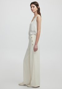 White satin top with V-neck, paired with high-waisted, wide-leg trousers in cream, featuring gold-button accents on the side.