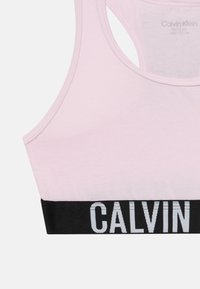 Svijetlo ružičasti sportski grudnjak s širokim crnim elastičnim remenom na kojem piše "CALVIN" bijelim slovima. Glatka tkanina i dizajn s izrezom na leđima.