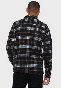 Camisa de franela a cuadros en blanco y negro con detalles en naranja, que presenta un cuello puntiagudo, mangas largas y puños con botones; textura suave.