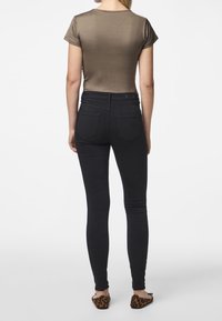 Ruskea lyhythihainen paita ja mustat tiukat farkut. Paita on sileä; farkuissa on takataskut. Jalkineissa on leopardikuosisuus.