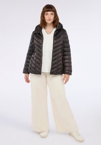 Giacca a vento nera con cappuccio, caratterizzata da una trama trapuntata e cuciture diagonali. Abbinata a un top bianco e pantaloni beige larghi.