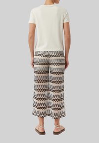 Witte katoenen t-shirt gecombineerd met gestreepte wijde broek met zigzaglijnen in bruin, beige en zwart. Draag met platte sandalen.