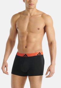 Svarta boxerkalsonger med enfärgad design, utrustade med ett orange elastiskt midjeband med svarta logodetaljer. Slät textur, figurnära passform.