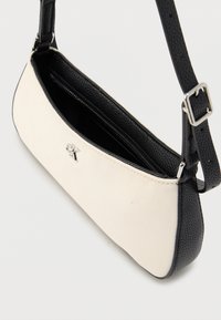 Μαύρη και λευκή τσάντα χειρός από δέρμα με υφή και καμβά, με κλείσιμο φερμουάρ και ρυθμιζόμενο ιμάντα ώμου, με μικρή λεπτομέρεια λογότυπου.