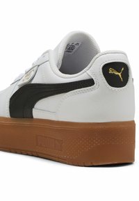 Baskets en cuir blanc avec accents noirs, semelle en caoutchouc couleur gomme et logo doré. Caractéristiques d'une finition lisse et d'un col rembourré pour le confort.