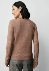 Hellbraunes Sweatshirt mit weicher Textur, langen Ärmeln und schmalem Saum, kombiniert mit karierter Hose. Schlichter Ausschnitt.