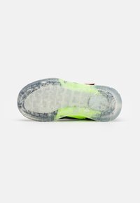 Clear outsole with textured pattern, vibrant green midsole, and red accents. Upper shows a mix of materials, primarily black.