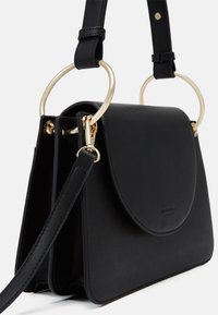 Musta nahkainen käsilaukku, jossa on pyöreä läppä, kultaiset pyöreät kahvat ja irrotettava hihna. Silkkinen pinta ja minimalistinen muotoilu.