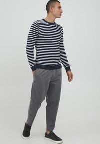 Marineblau-weiß gestreifter Pullover, mit gerippten Bündchen, kombiniert mit grauen schmal geschnittenen Jogginghosen und schwarzen Sneakers, zeigt ein lässiges Outfit.