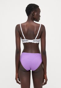 Purple cotton high-waisted briefs with scalloped trim paired with a white lace-trimmed bra featuring adjustable straps.
