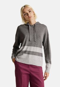 Mikina s kapucí v tmavě šedé barvě se světle šedými horizontálními pruhy. Měkká pletená látka, žebrované manžety a lem, volný střih a klokaní kapsa.