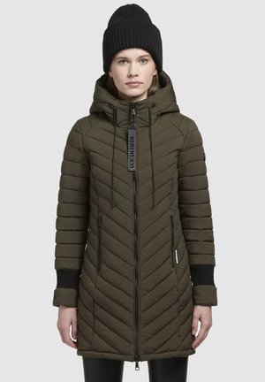 Olive green puffer coat with a chevron pattern, high collar, zip closure, adjustable hood, and black ribbed cuffs. Paired with a black knit beanie.
