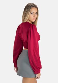 Bordeaux crop top met lange pofmouwen en gestructureerde stof, gecombineerd met een hoge taille grijze minirok, weergegeven vanaf de zijkant.
