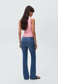 Top rosa sin mangas combinado con jeans de mezclilla azul acampanados. Los jeans tienen un corte clásico con bolsillos traseros visibles y un ligero desvanecimiento.