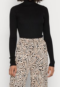 Svart ribbad polotröja i kombination med byxor i beige och svart med abstrakt mönster, som har elastisk midja och dragsko.