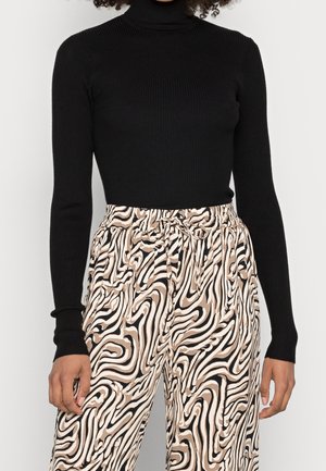 Maglione nero a costine con colletto alto abbinato a pantaloni beige e neri con motivo astratto, dotati di cintura elasticizzata e cordoncino.