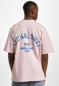 Lyserosa bomull t-skjorte, oversized passform, med blå tekst: "JACK&JONES EDTN EST.1990 NORDIC ACTIVE CREW" på baksiden. Myk tekstur.