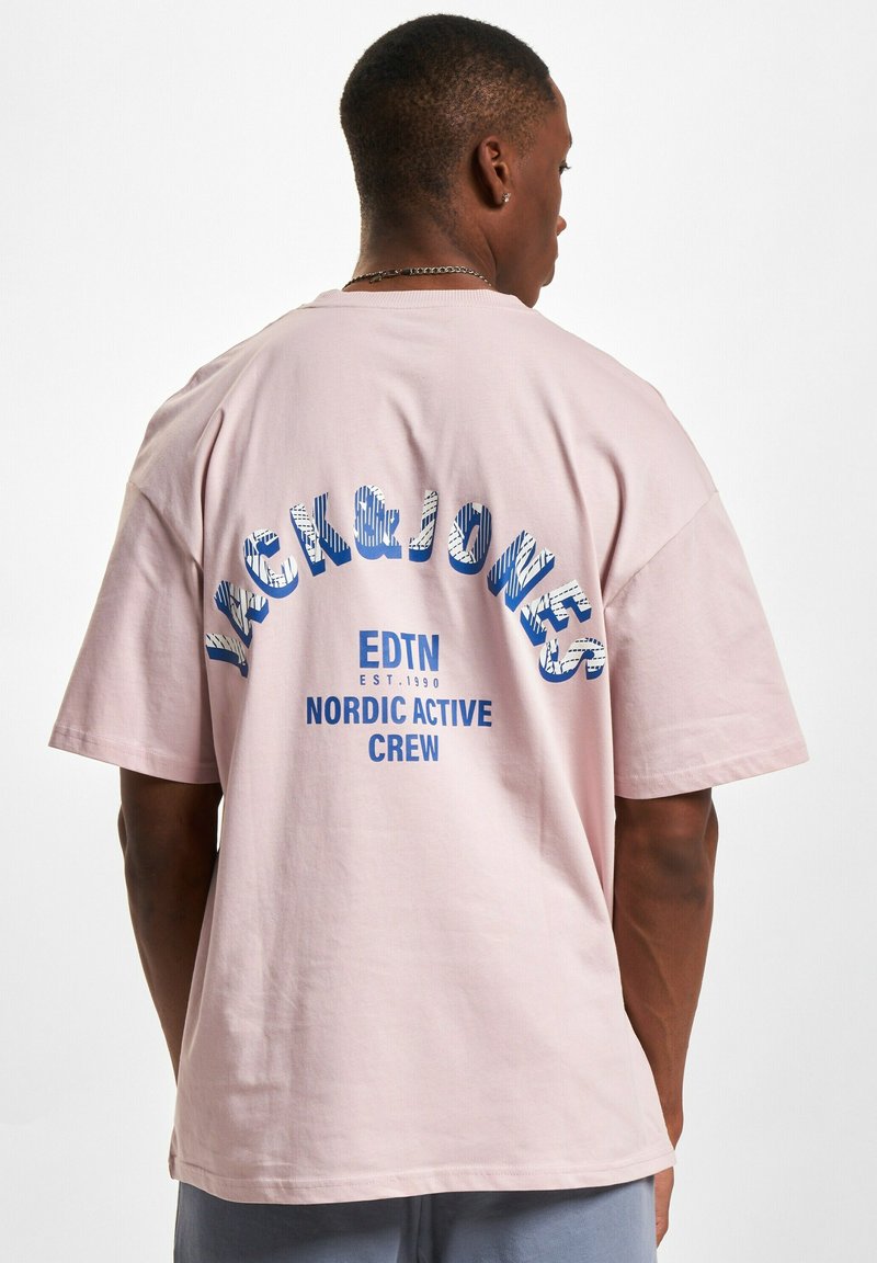 Lyserosa bomull t-skjorte, oversized passform, med blå tekst: "JACK&JONES EDTN EST.1990 NORDIC ACTIVE CREW" på baksiden. Myk tekstur.