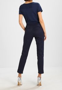 Marinblå t-shirt med rund halsringning, kombinerad med åtsittande marinblå byxor och silverfärgade högklackade skor, visad bakifrån.