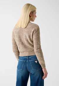 Pull beige en maille avec motif texturé, ourlet côtelé et manches longues, associé à un jean bleu taille haute avec poches arrière.