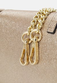 Bolso metálico dorado con una superficie texturizada. Cuenta con un asa de cadena dorada gruesa y dos clips metálicos resistentes.