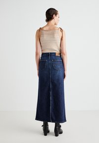 Striped knit tank top with tie straps paired with a long dark blue denim skirt featuring back pockets and yellow stitching. Black heeled ankle boots.