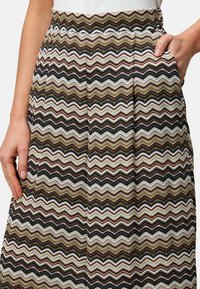 Jupe à motif ondulé en crème, marron et noir. Fabriquée en tissu texturé avec des poches latérales et des plis à la taille pour une touche de style supplémentaire.