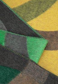 Manta de lana multicolor con patrones geométricos en verde, amarillo, gris y marrón, con una textura suave y bordes finamente cosidos.