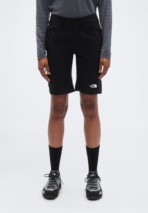 Fekete rövidnadrág gombos záródással és két cipzáras zsebbel, a North Face logójával az alsó lábszáron. Fekete zoknival és cipővel viselve.