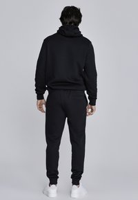 Czarny zestaw z bluza z kapturem i dresami, wykonany z miękkiego materiału, z ribbowanymi mankietami i kapturem. Dresy mają tylną kieszeń i zwężają się przy kostkach.