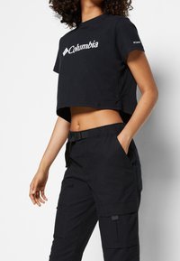 Svart kortärmad t-shirt med vitt "Columbia"-logotyp på framsidan, i kombination med svarta cargobyxor som har fickor och en justerbar midja.
