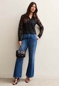 Czarna koronkowa bluzka z cekinami, niebieskie dżinsowe spodnie z wysokim stanem i szerokimi nogawkami, oraz czarna torebka z cekinami na łańcuszku. Czarne sandały na obcasie.