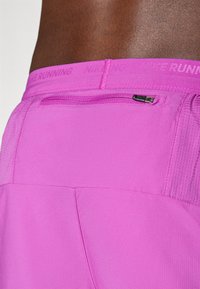 Magenta Laufshorts aus textured Stoff, mit einer kleinen Reißverschlusstasche und einem markierten Bund, entworfen für sportliche Aktivitäten.