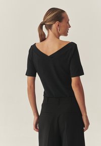 Čierny krátky top s textúrovaným povrchom a výstrihom do tvaru V, s prispôsobeným strihom, ktorý dokonale ladí s elegantnými čiernymi nohavicami.