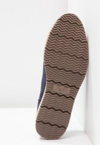Semelle de chaussure montrant une tige bleu marine avec des détails cousus, une semelle extérieure en caoutchouc beige et un motif de grip en zigzag, taille indiquée comme 37.