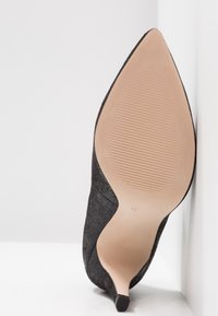 Chaussure à talons aiguilles noire à bout pointu avec un supérieur en tissu texturé, semelle en caoutchouc tan et motif ribbé subtil sur la semelle pour l'adhérence. Taille 43.