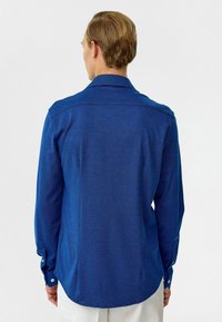 Blauw overhemd met lange mouwen, gemaakt van een soepele stof, met knoopmanchetten en een klassieke kraag. Heeft een subtiel heatherpatroon en een gebogen zoom.