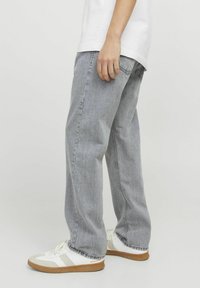 Jeans de mezclilla gris claro con un corte holgado, costuras visibles y bolsillos laterales. Combinados con zapatillas blancas con detalles grises y suelas de goma.