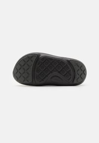 Black rubber shoe sole with textured grip pattern, featuring rounded toe and distinct tread design for traction and durability.