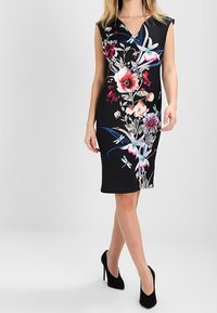 Musta mekko, jossa on kukkakuosi punaisena, vaaleanpunaisena ja sinisenä. Lyhyet hihat, V-aukko ja vartalonmyötäinen malli. Yhdistetty mustiin korkokenkiin.