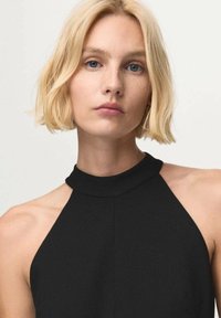 Top negro con cuello halter que presenta un alto cuello, un corsé ajustado y una textura de tela suave. Diseño minimalista sin patrones visibles ni herrajes.
