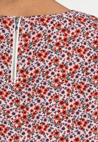 Top floreale con sfondo bianco decorato da piccoli fiori rossi, viola e neri, e una zip argentata visibile sullo scollo posteriore.
